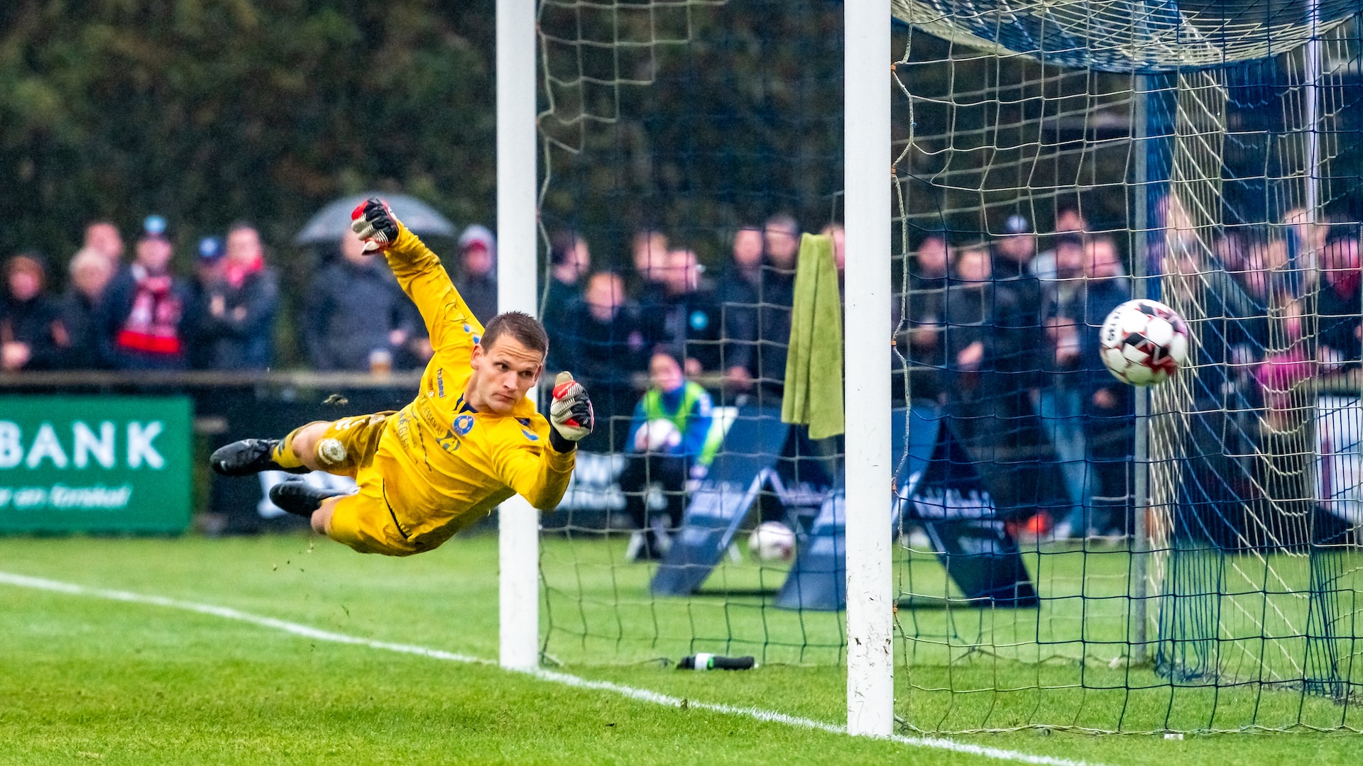 Action shot of goalie in yellow jersey diving to block a goal attempt